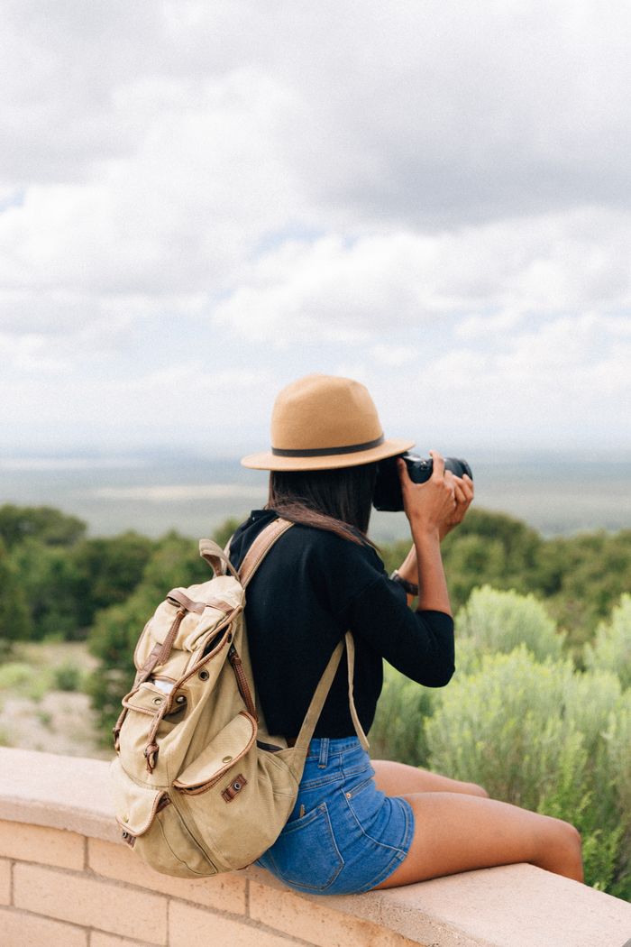 A woman in casual attire captures a scenic view with her camera from a ledge.