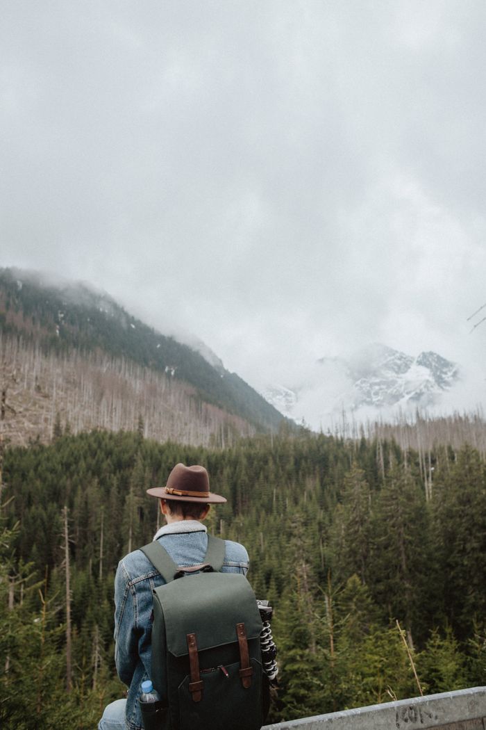 services-01 Adult man in a denim jacket sits facing snowy mountains, evoking wanderlust and serenity.